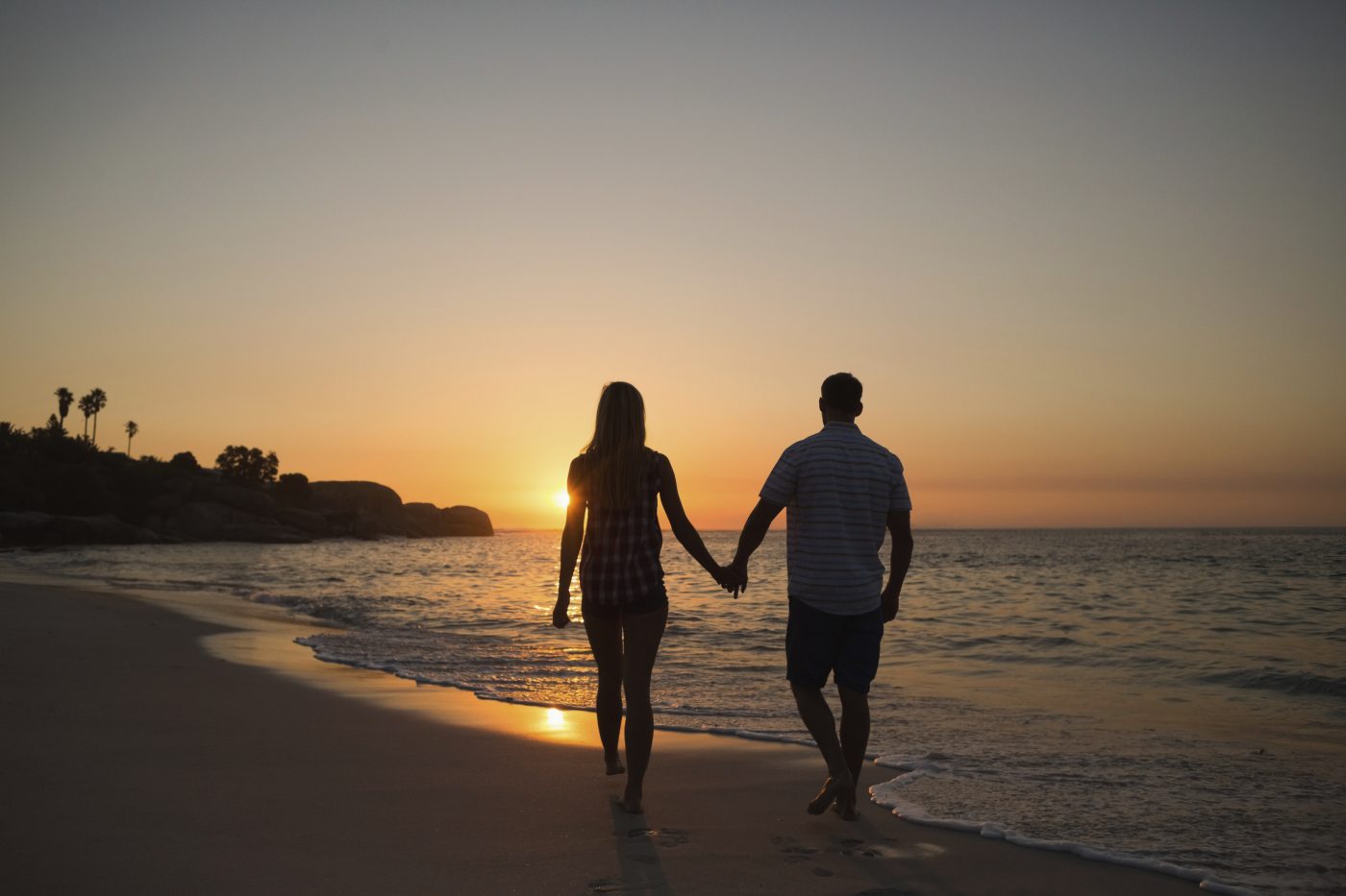 couple holding hands while walking on beach