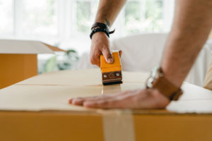 person closing cardboard box with packing tape