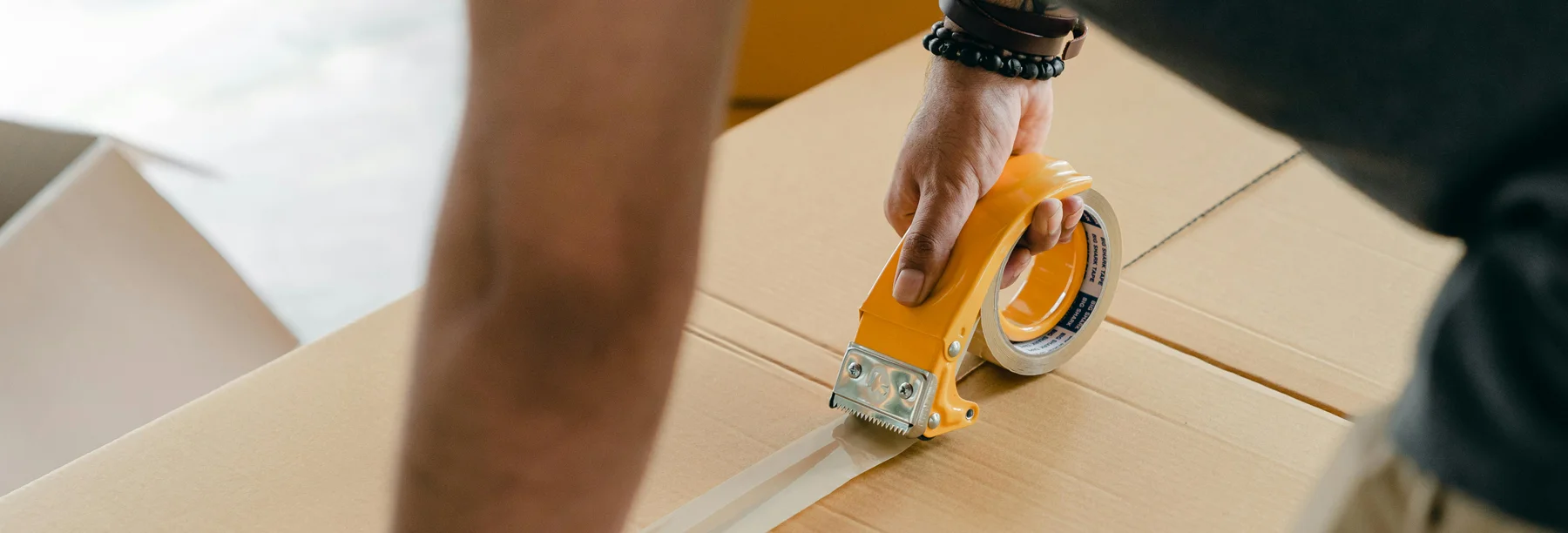 Person sealing a box with tape, preparing and packing food for moving to a new location.